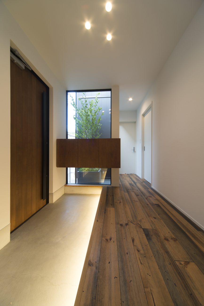 足元に間接照明が取り付けられた大きな窓があるモルタルの玄関・デザイン住宅