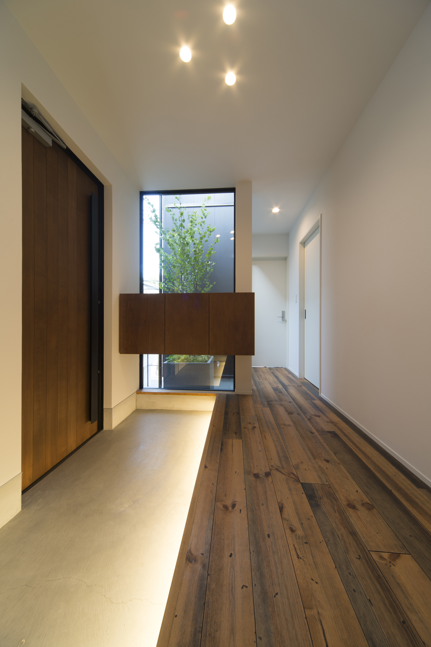 足元に間接照明が取り付けられた大きな窓があるモルタルの玄関・デザイン住宅