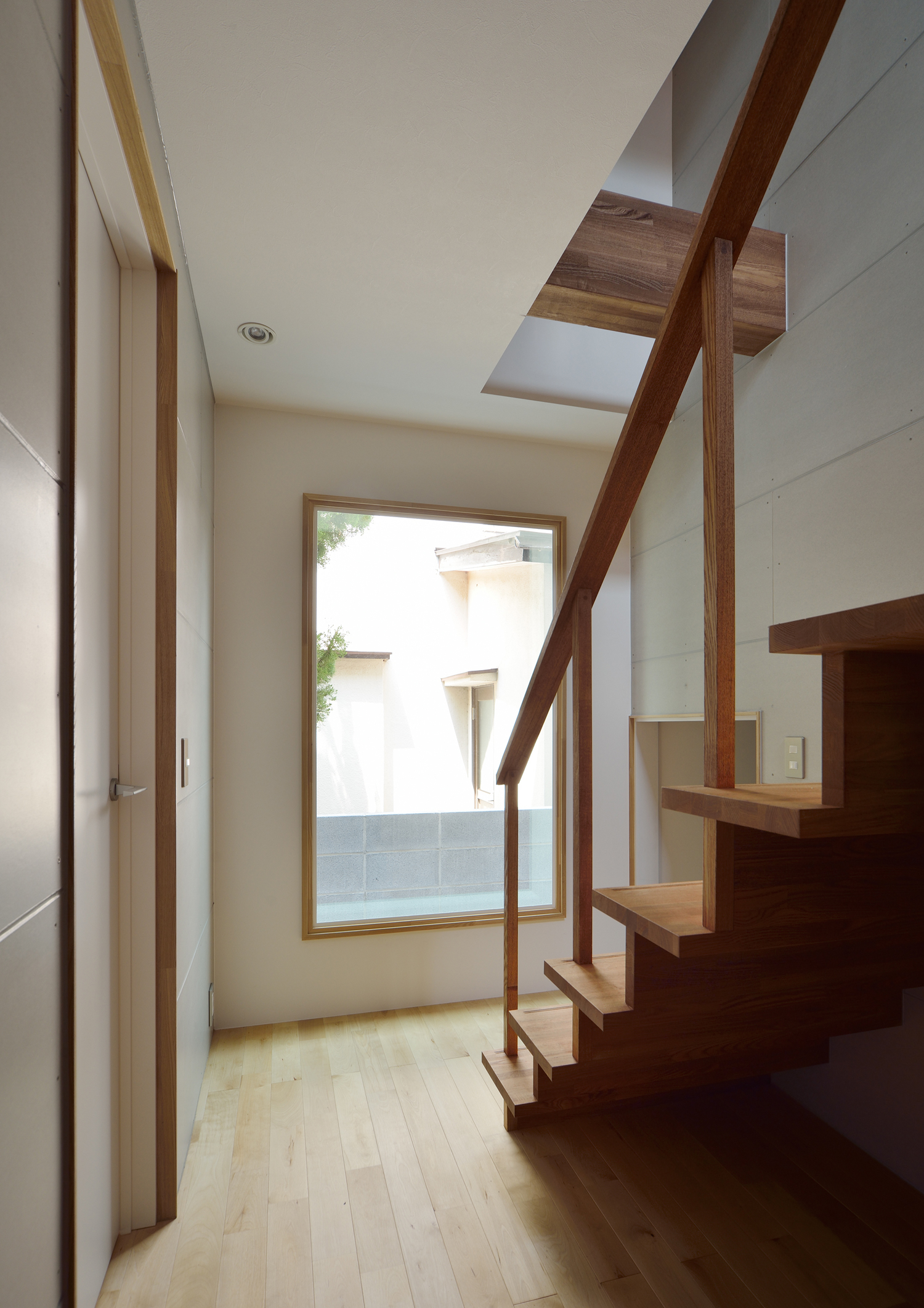 突き当りに大きな窓がある木のスケルトン階段がある廊下・デザイン住宅