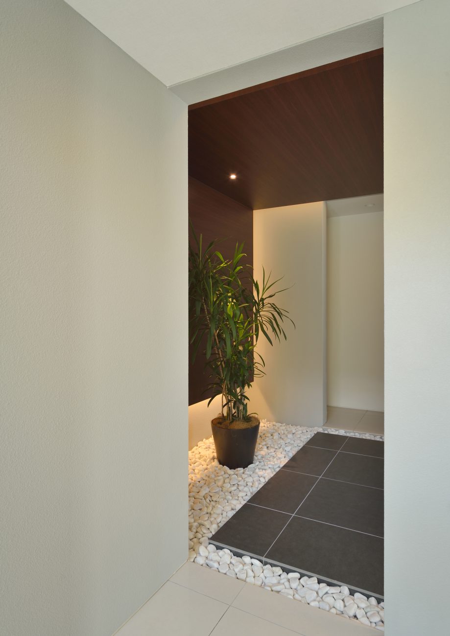 敷石や観葉植物があるホテルのエントランスのような木目の天井の玄関・デザイン住宅