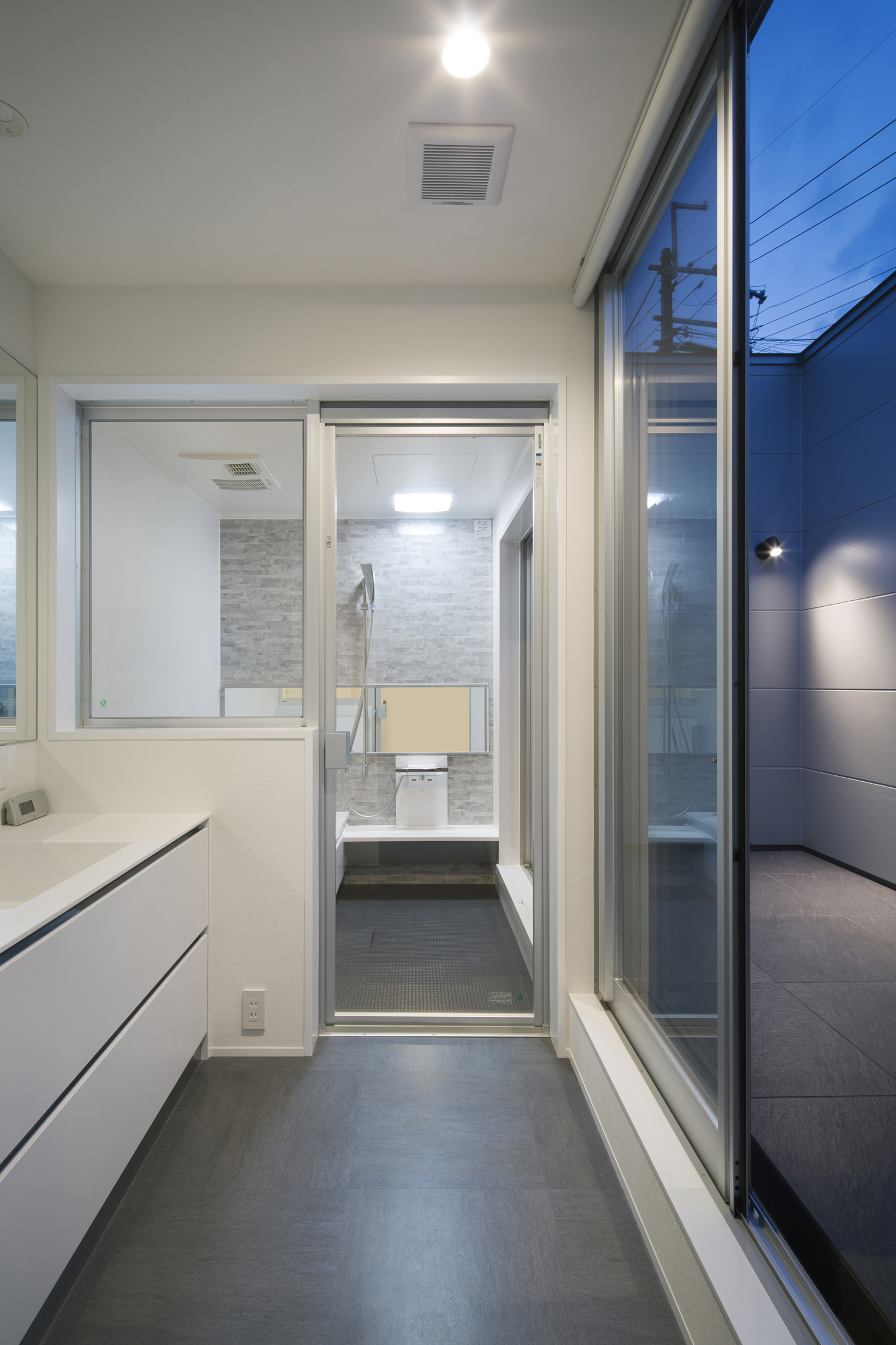 ガラス扉付きの浴室があるテラスに面した明るい洗面所・デザイン住宅