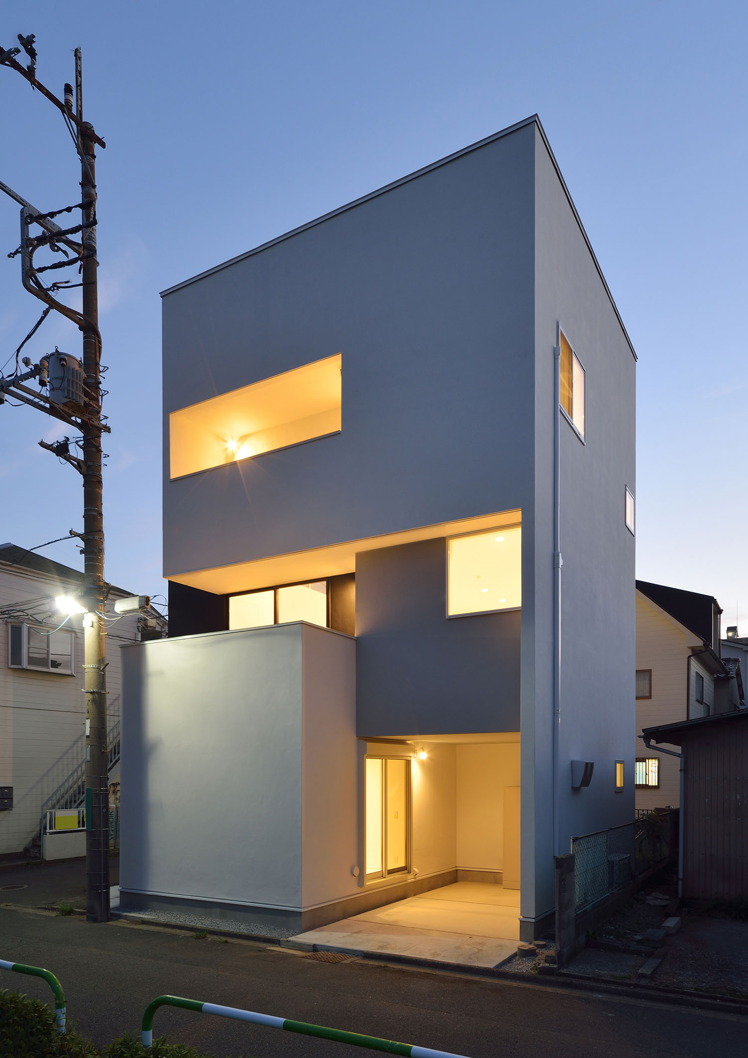 インナーガレージやバルコニーが照明に照らされた白いキューブ状の外観の家・デザイン住宅