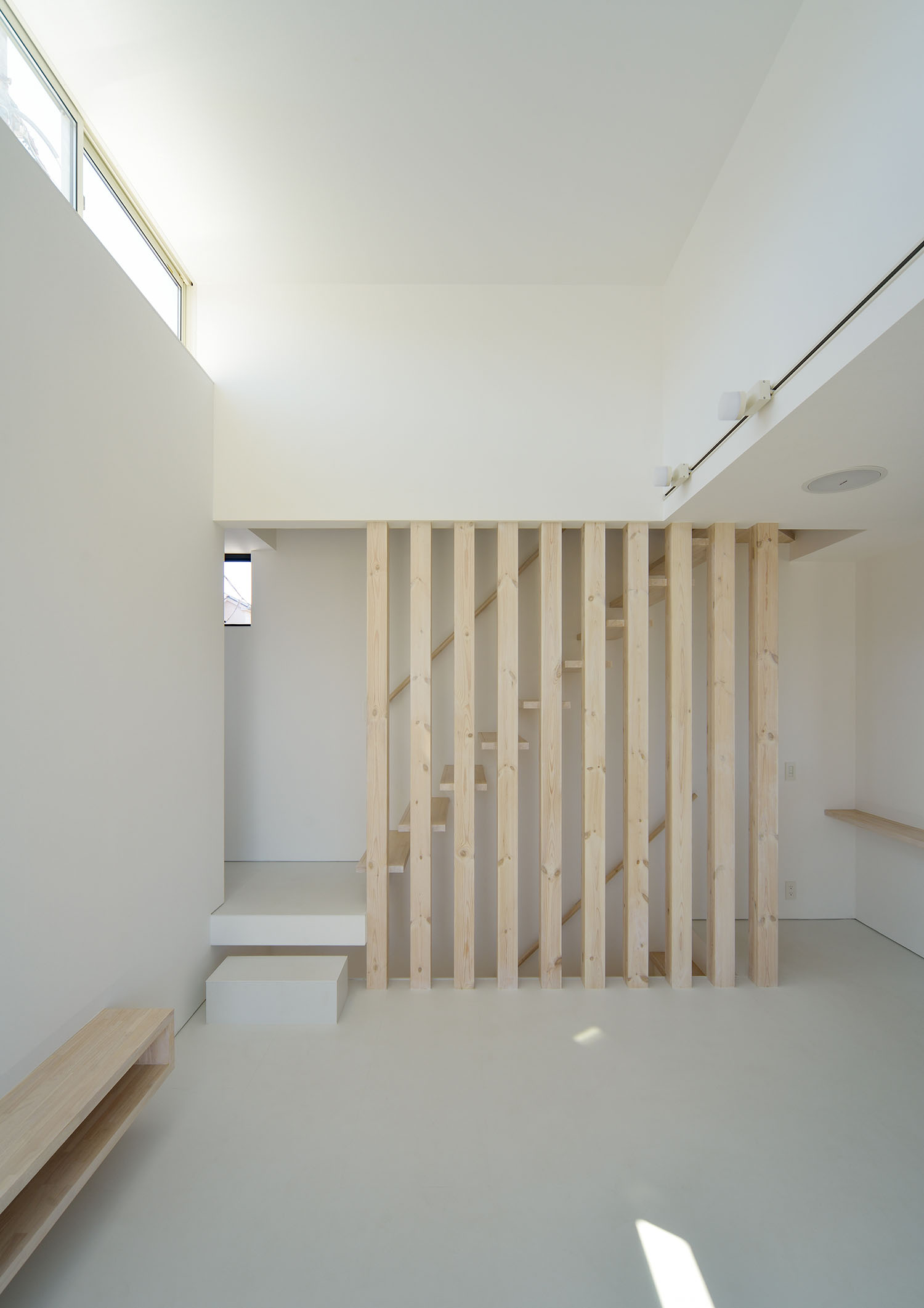 階段室に木のルーバーが取り付けられた白い壁で高天井のLDK・デザイン住宅
