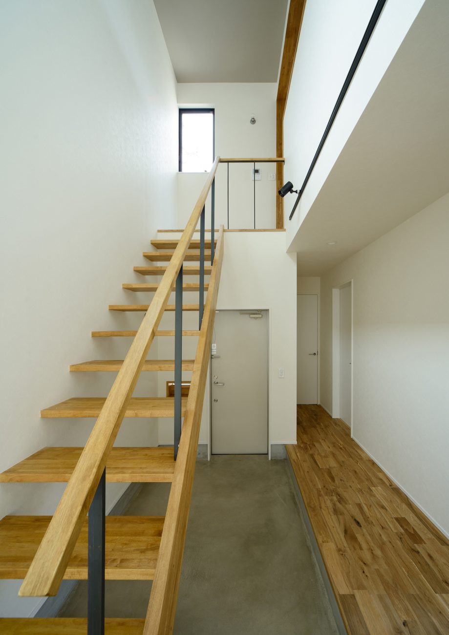 モルタルの土間玄関にある木のスケルトン階段・デザイン住宅