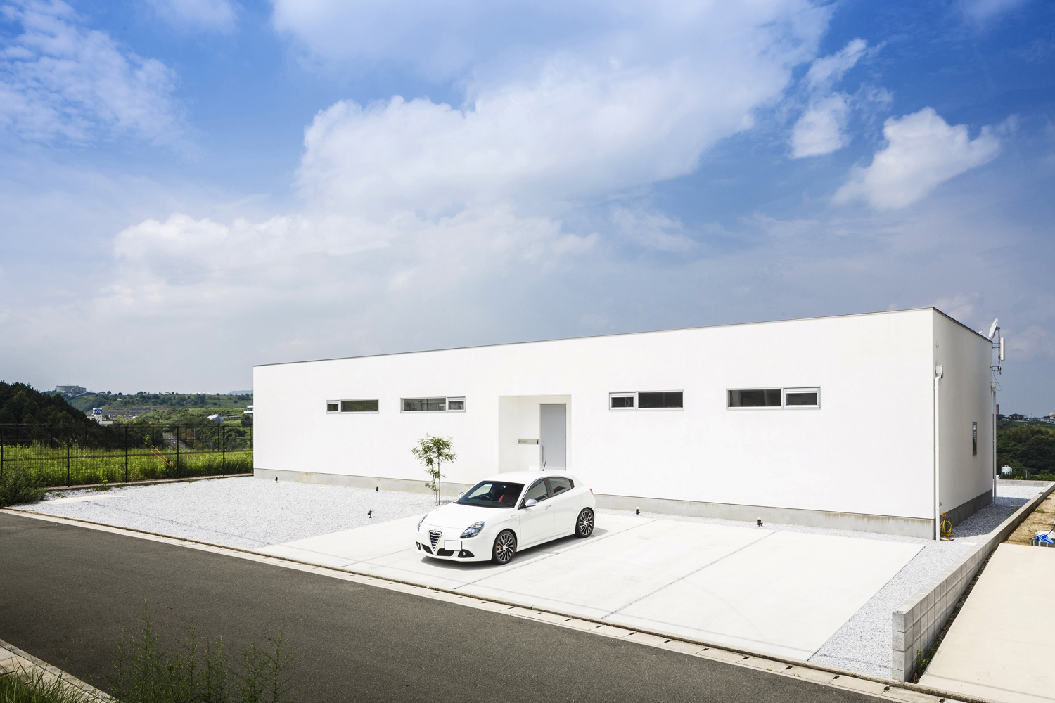開けた土地に建つ白いスクエアな外観で広い駐車場がある平屋・デザイン住宅