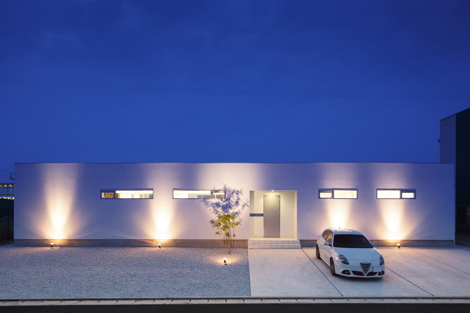 床に取り付けられた照明に照らされる白い外壁の平屋住宅・デザイン住宅