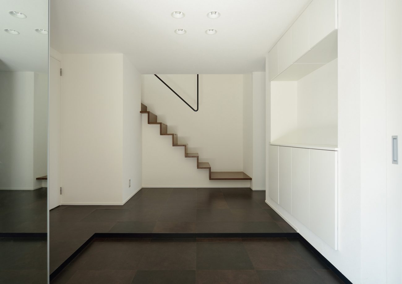 正面にシンプルな階段がある白い壁と黒い床の玄関・デザイン住宅