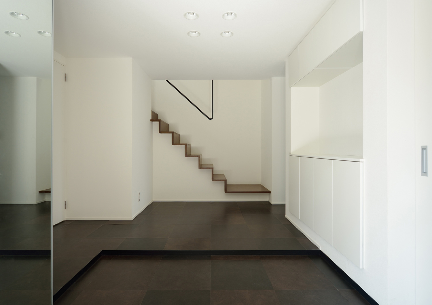 正面にシンプルな階段がある白い壁と黒い床の玄関・デザイン住宅