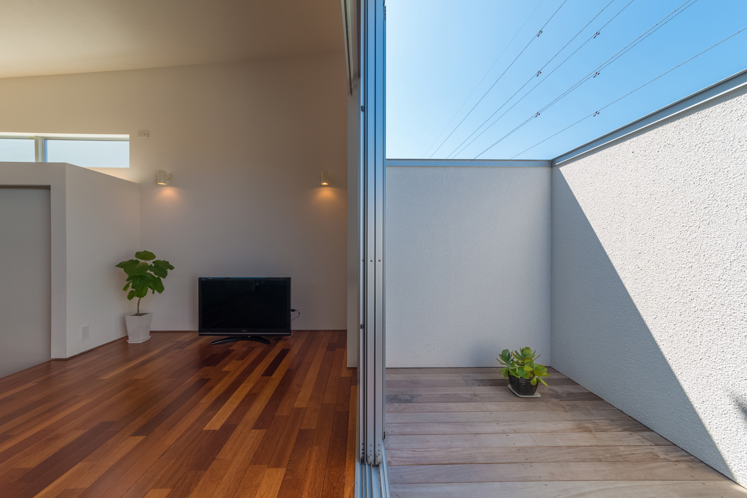 高い目隠し壁があるLDKとフラットに繋がるウッドデッキのテラス・デザイン住宅