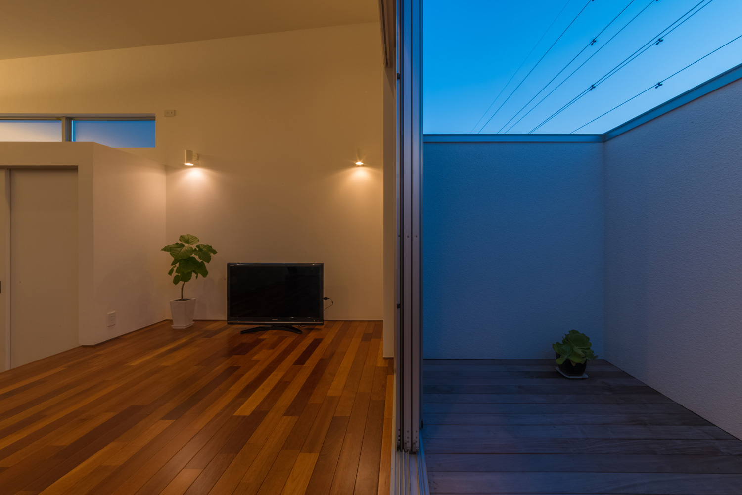 壁に間接照明が取り付けられたLDKとフラットに繋がる高い目隠し壁付きのLDK・デザイン住宅