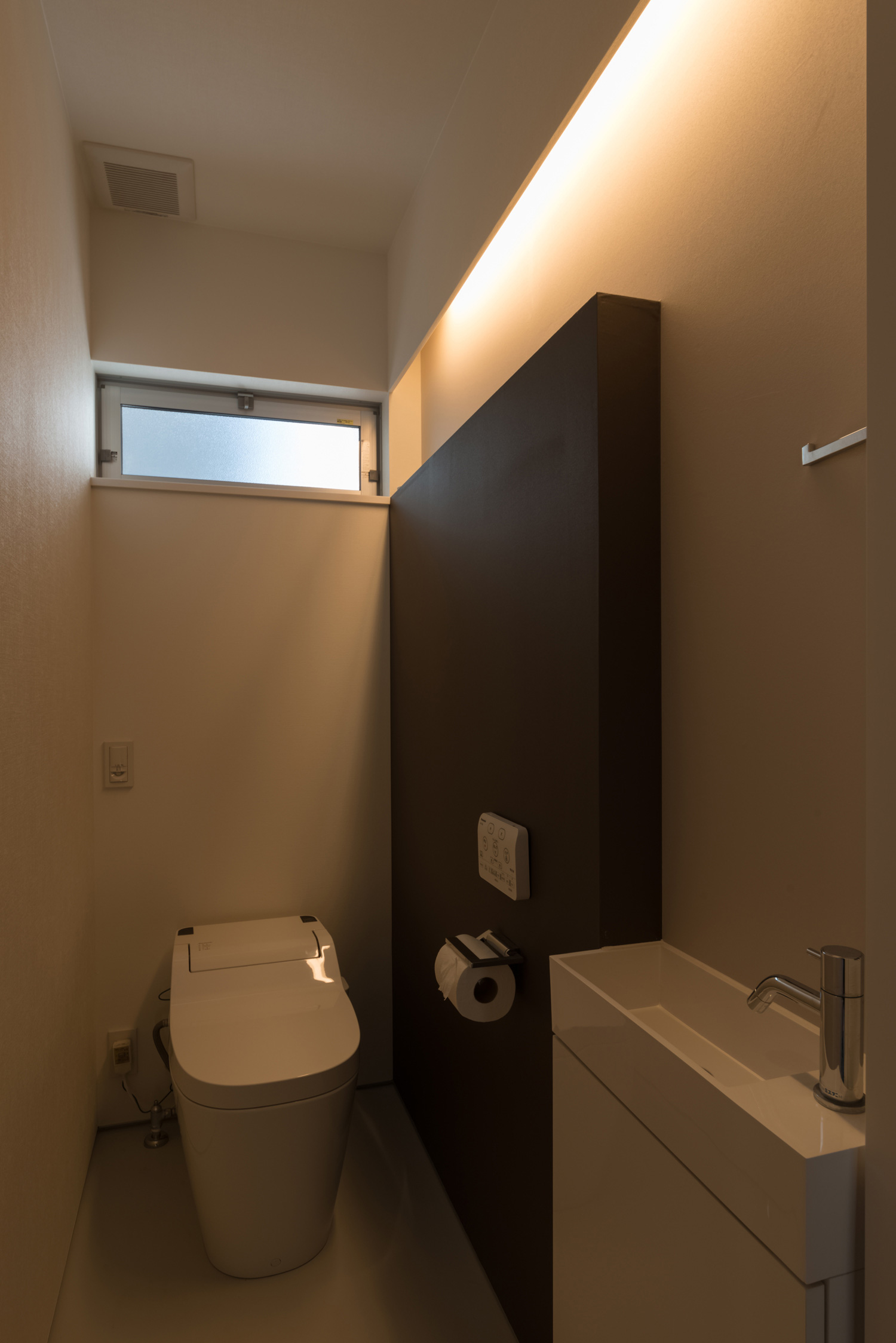 壁にライン状の間接照明を取り付けた薄型手洗いのあるトイレ・デザイン住宅