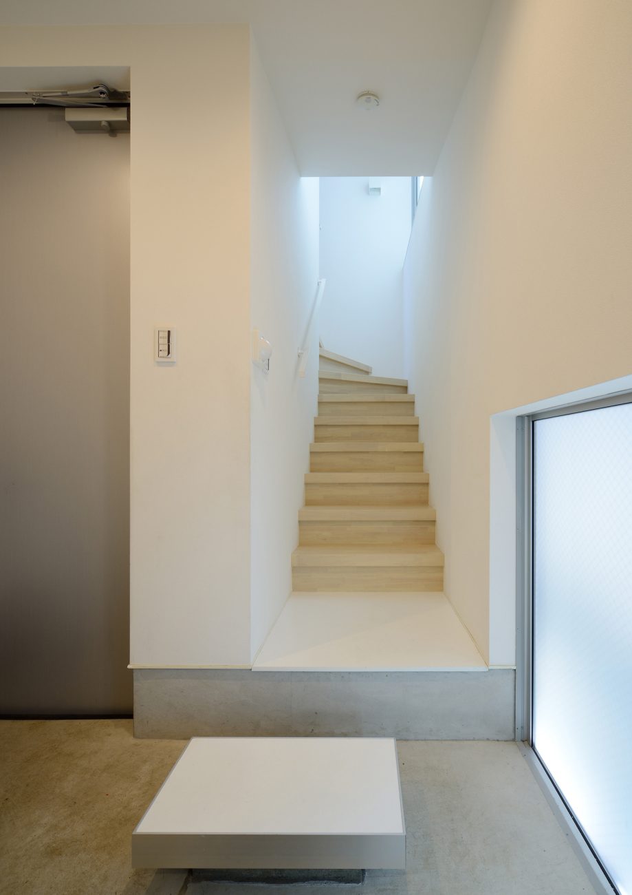 玄関のそばにある白い壁に挟まれた木の箱型階段・デザイン住宅