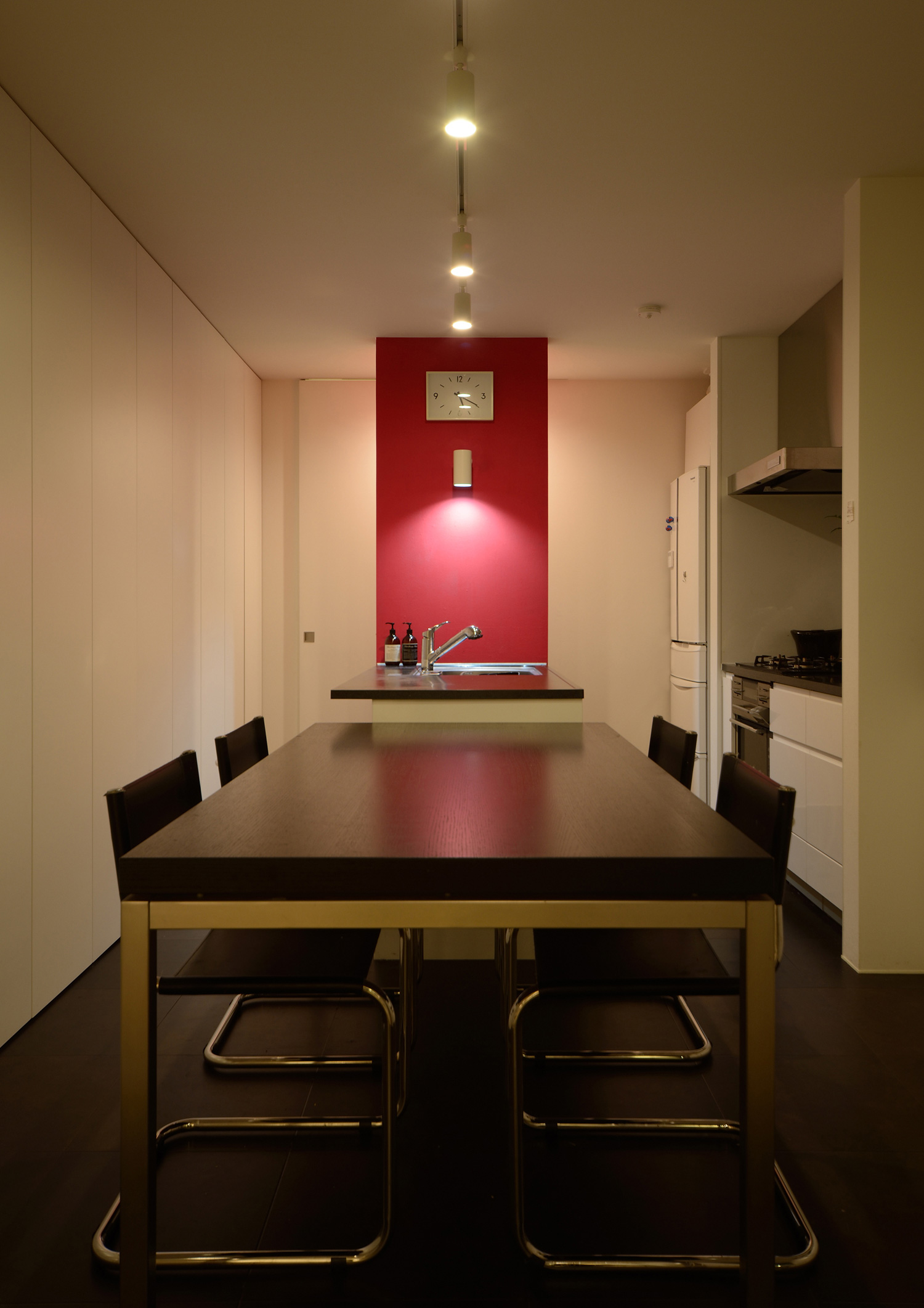 赤いアクセントウォールがアクセントになった黒いⅡ型キッチンとダイニングテーブル・デザイン住宅