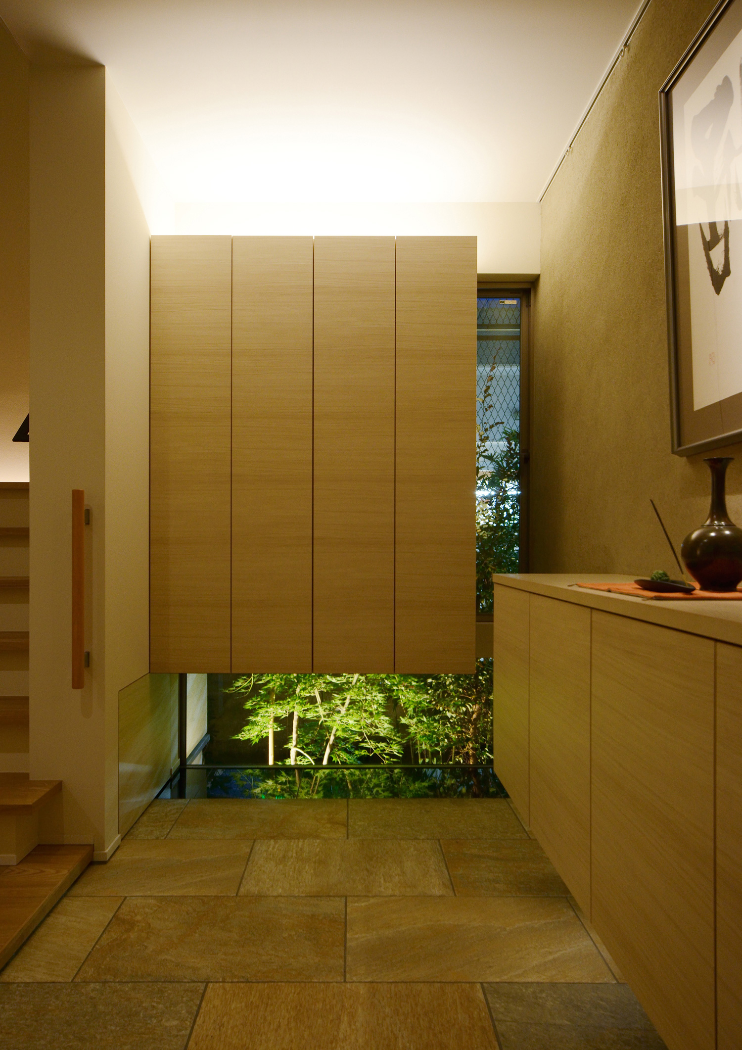 間接照明付きの浮いたデザインのシューズボックスや、植栽が見える窓がある玄関・デザイン住宅