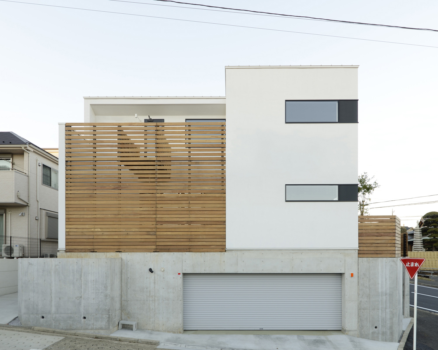 シャッター付きのインナーガレージと木のルーバーの目隠しがあるシンプルな外観の家・デザイン住宅