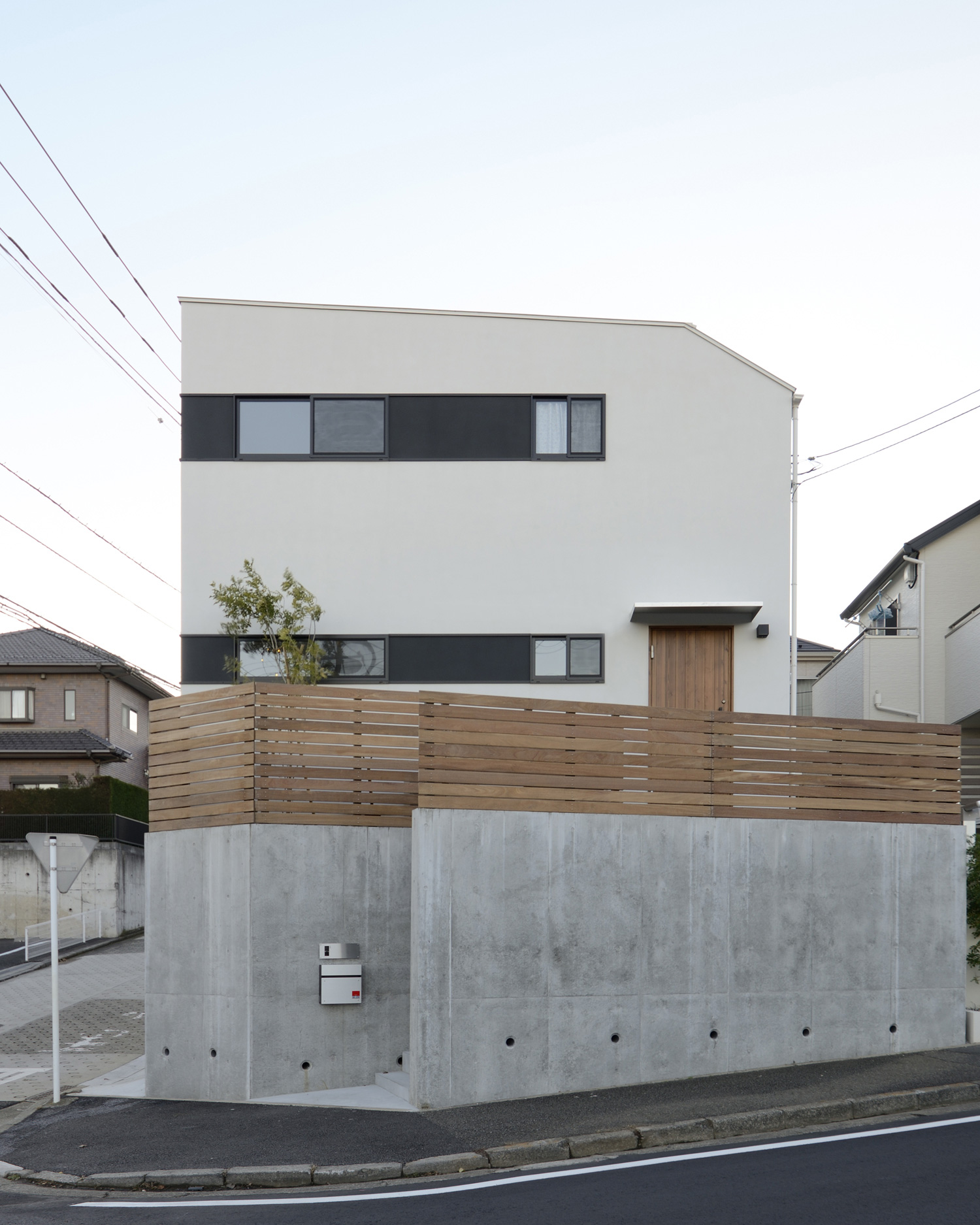 白い外壁に木のルーバーの目隠しが取り付けられている地下車庫付きの家・デザイン住宅