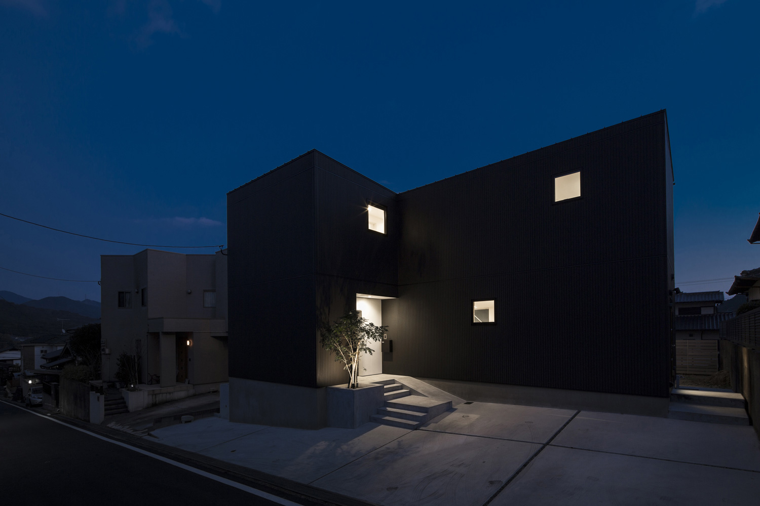 コンクリートの駐車場がある黒いキューブ状の外観の家・デザイン住宅