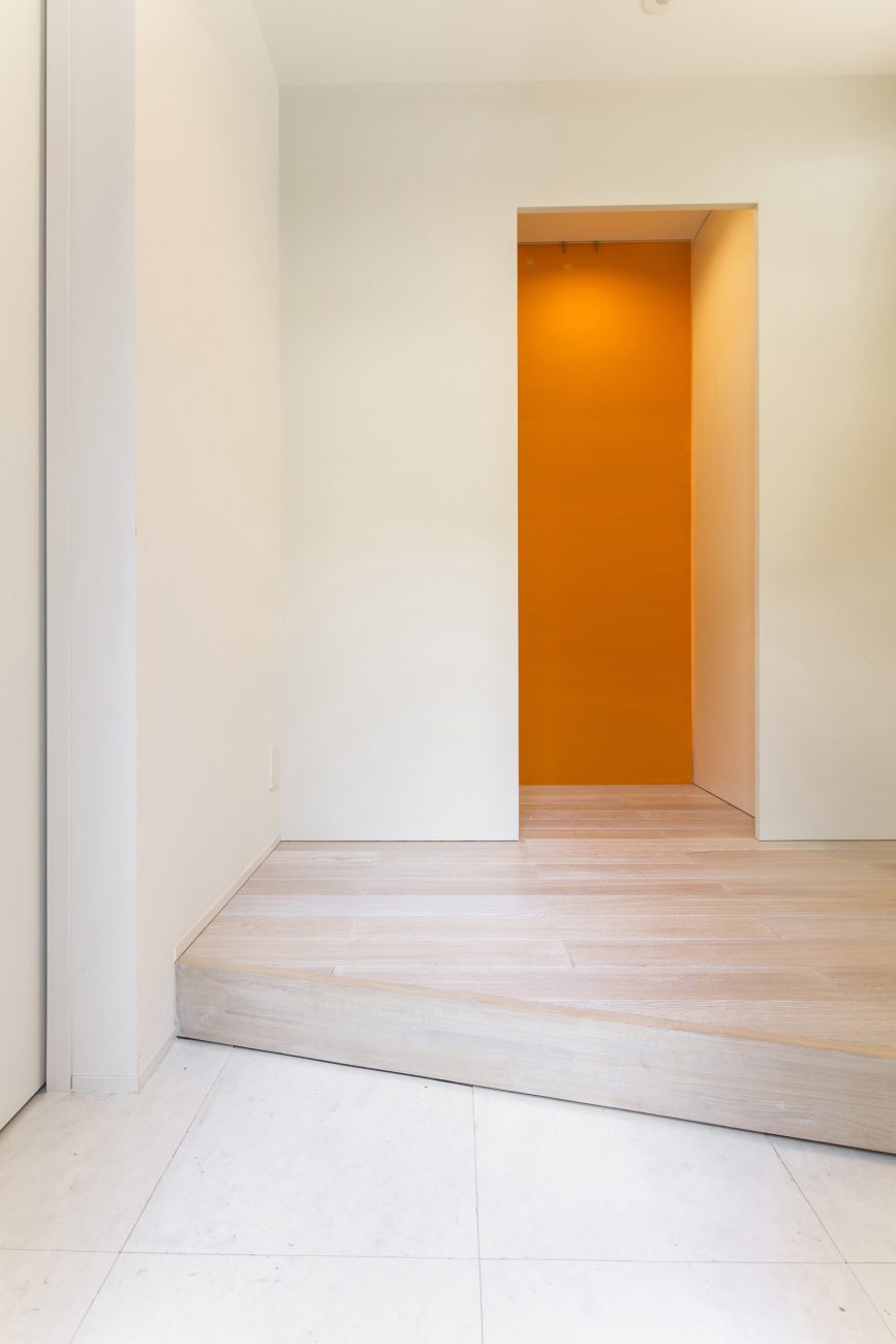 オレンジのクロスがアクセントになった白い壁のシンプルな玄関・デザイン住宅