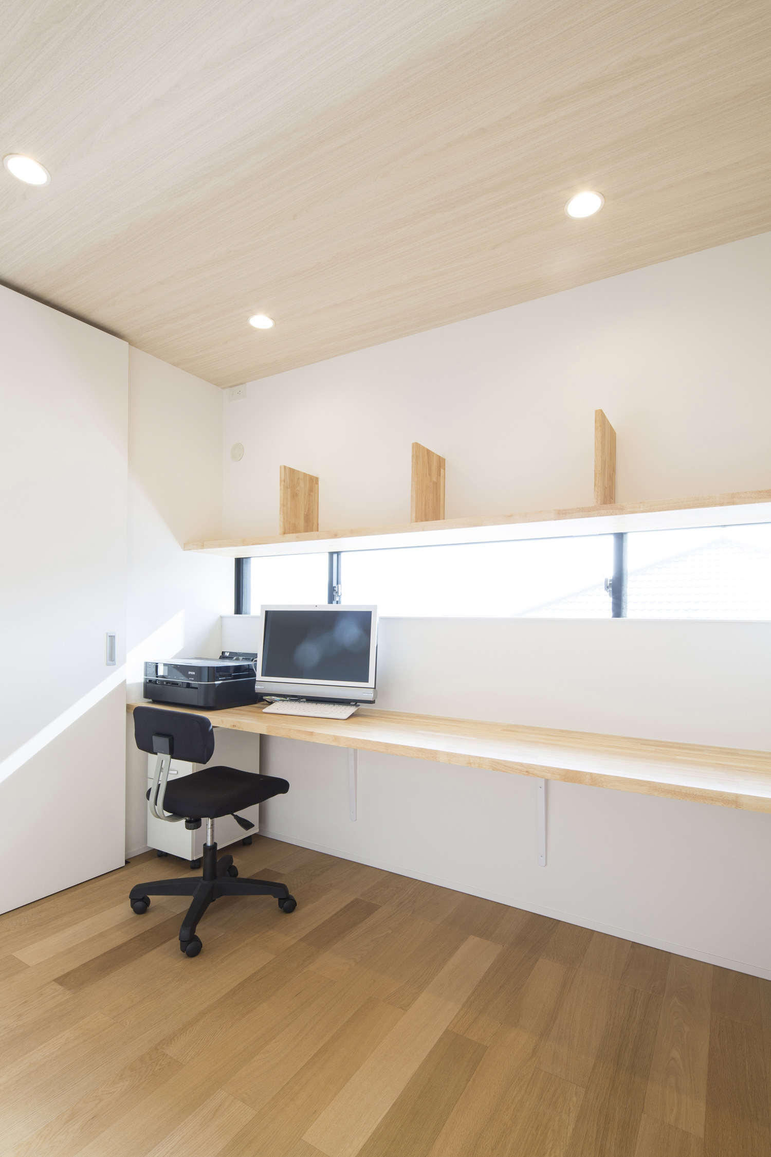 壁付けのデスクと本棚があるスリット窓付きのシンプルな書斎・デザイン住宅