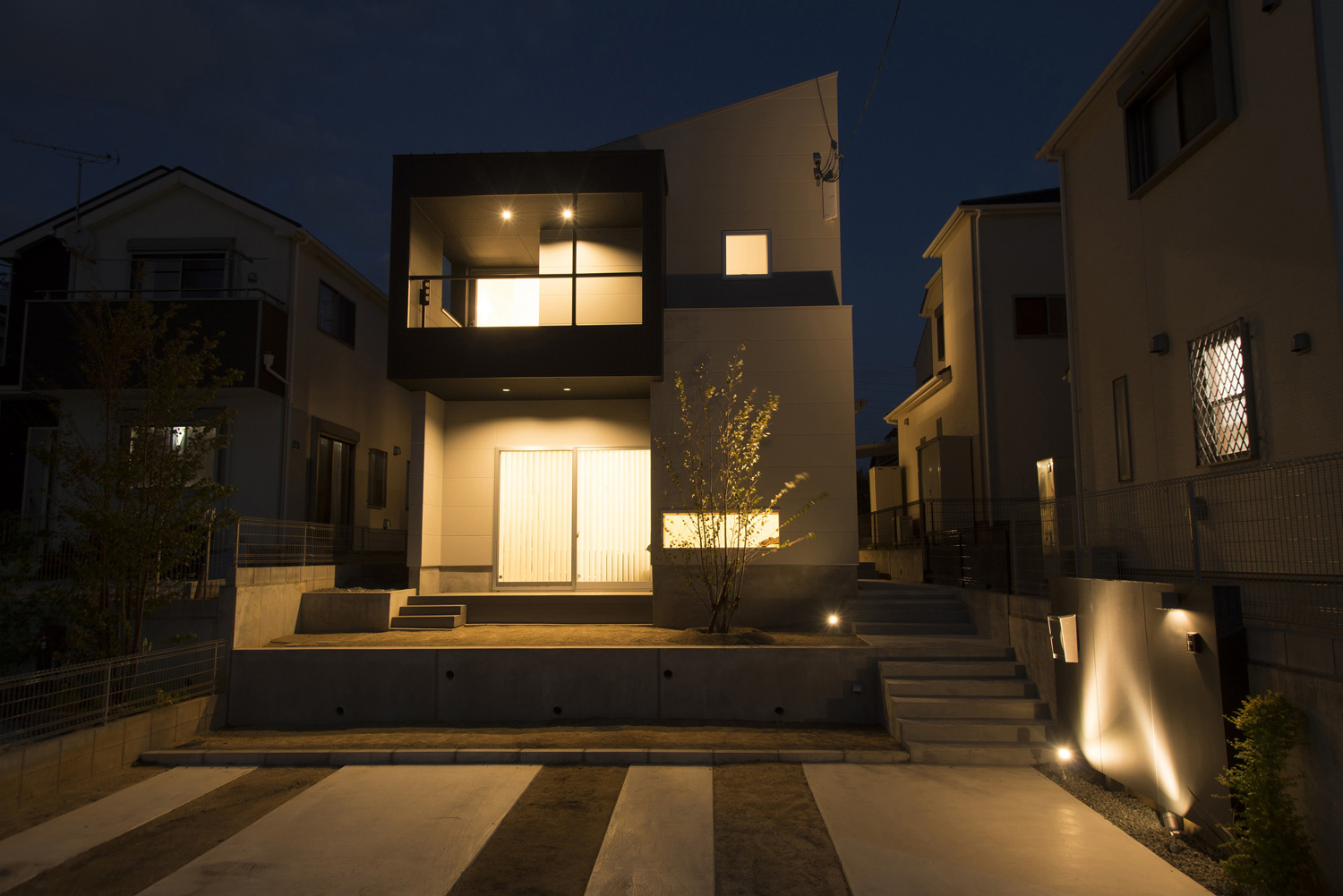 大きな窓とバルコニーから光が漏れるおしゃれな家の外観・デザイン住宅