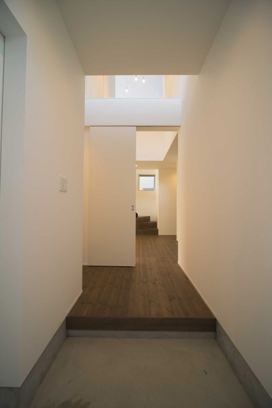 正面に吹き抜けの廊下がある白い壁に囲まれたシンプルな玄関・デザイン住宅