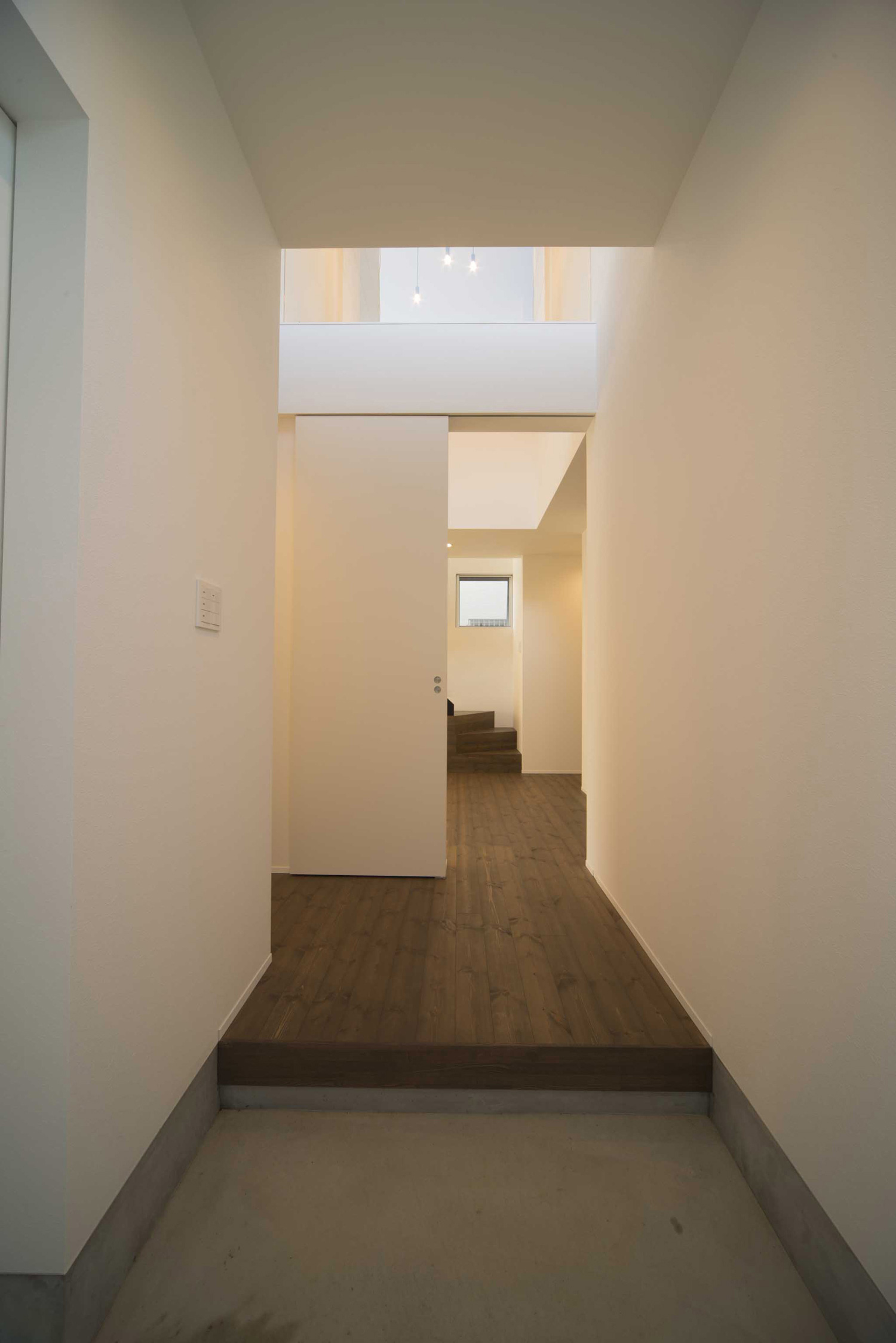 正面に吹き抜けの廊下がある白い壁に囲まれたシンプルな玄関・デザイン住宅