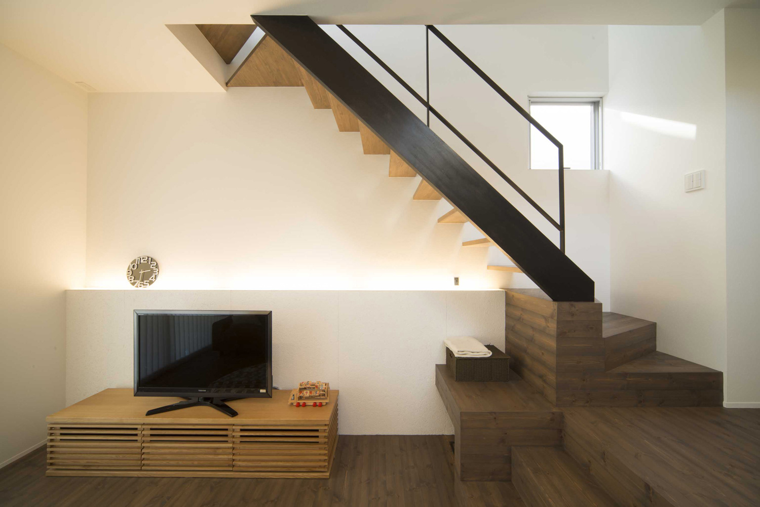 壁際に間接照明を取り付けた、階段下のスペースにテレビを置いたLDK・デザイン住宅