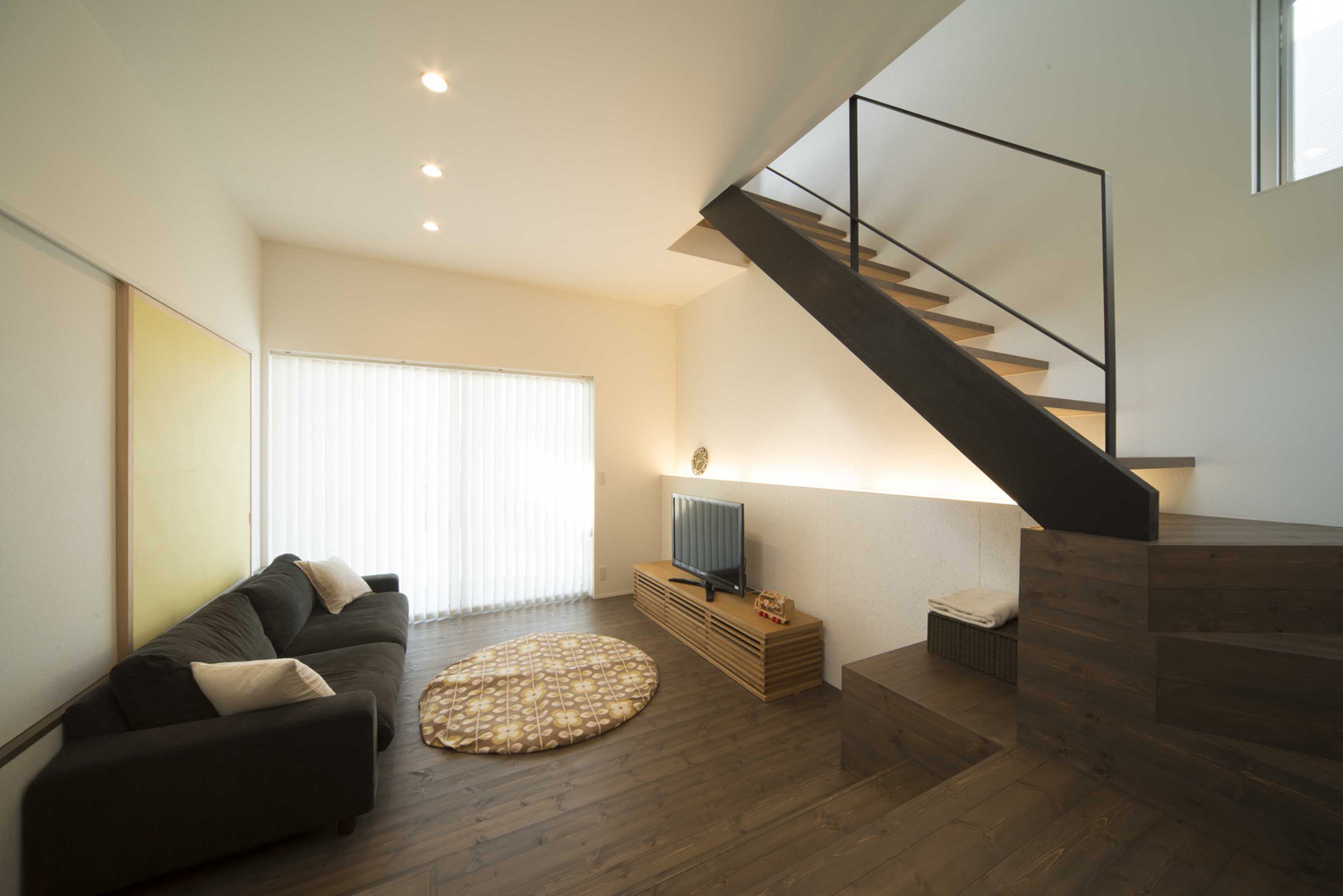 濃い色のフローリングでブラインド付きの大きな窓がある落ち着きのあるLDK・デザイン住宅