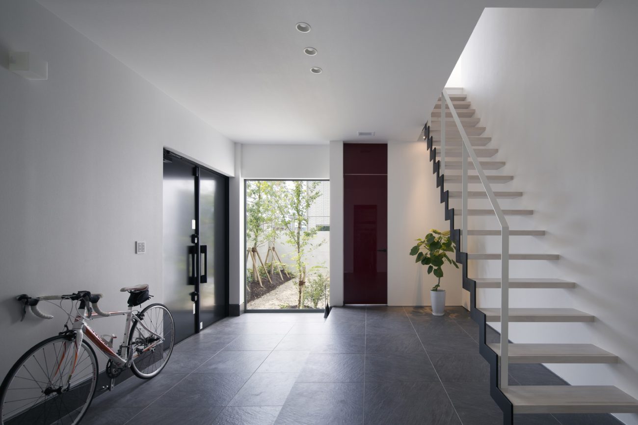 大きな窓から植栽が見える玄関とスケルトン階段のある廊下・デザイン住宅