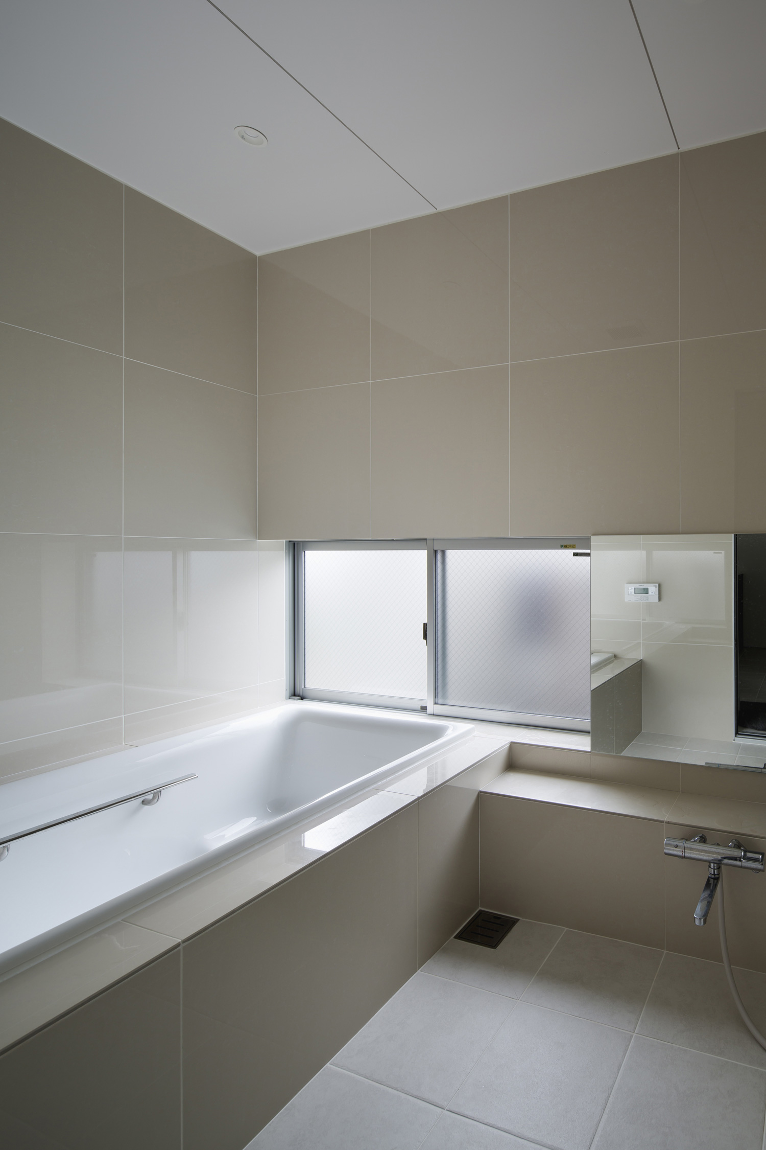 小窓を取り付けたベージュのタイルの浴室・デザイン住宅