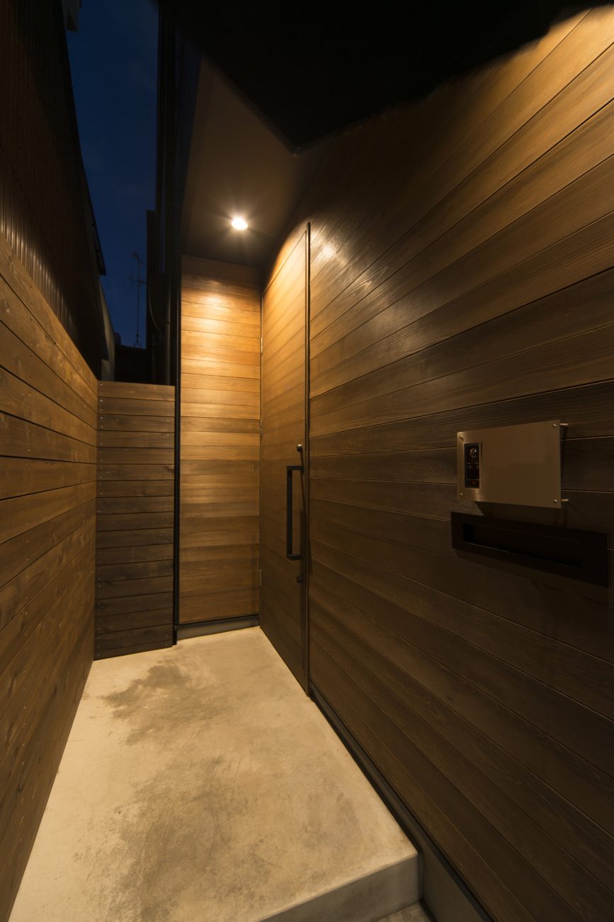 木の壁に木の玄関扉を取り付けたシンプルな玄関アプローチ・デザイン住宅