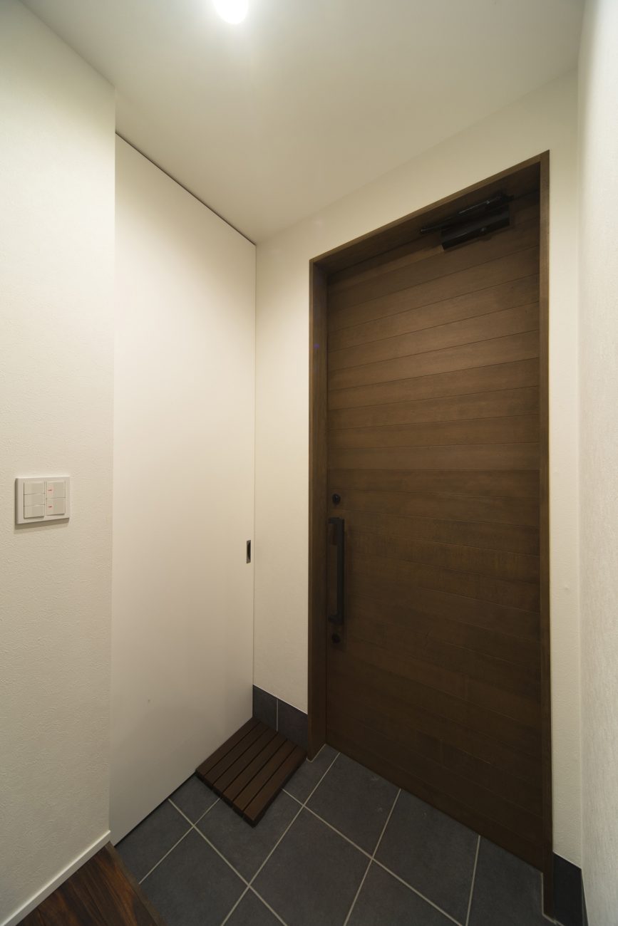 扉付きのシューズインクローゼットがある木目の玄関扉がある玄関・デザイン住宅