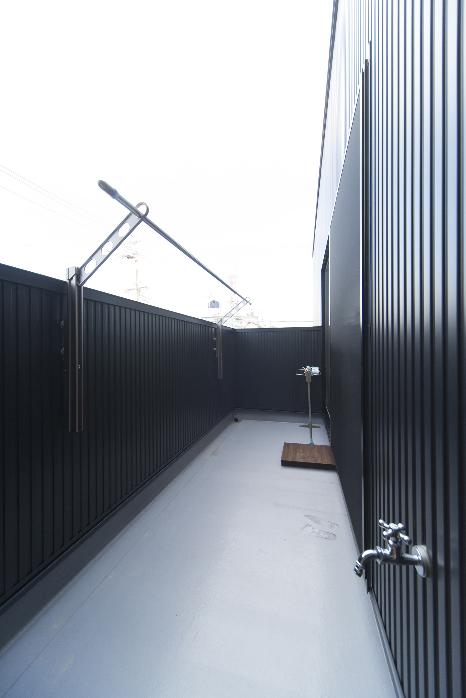 物干し金具を取り付けた黒い壁に囲まれたバルコニー・デザイン住宅