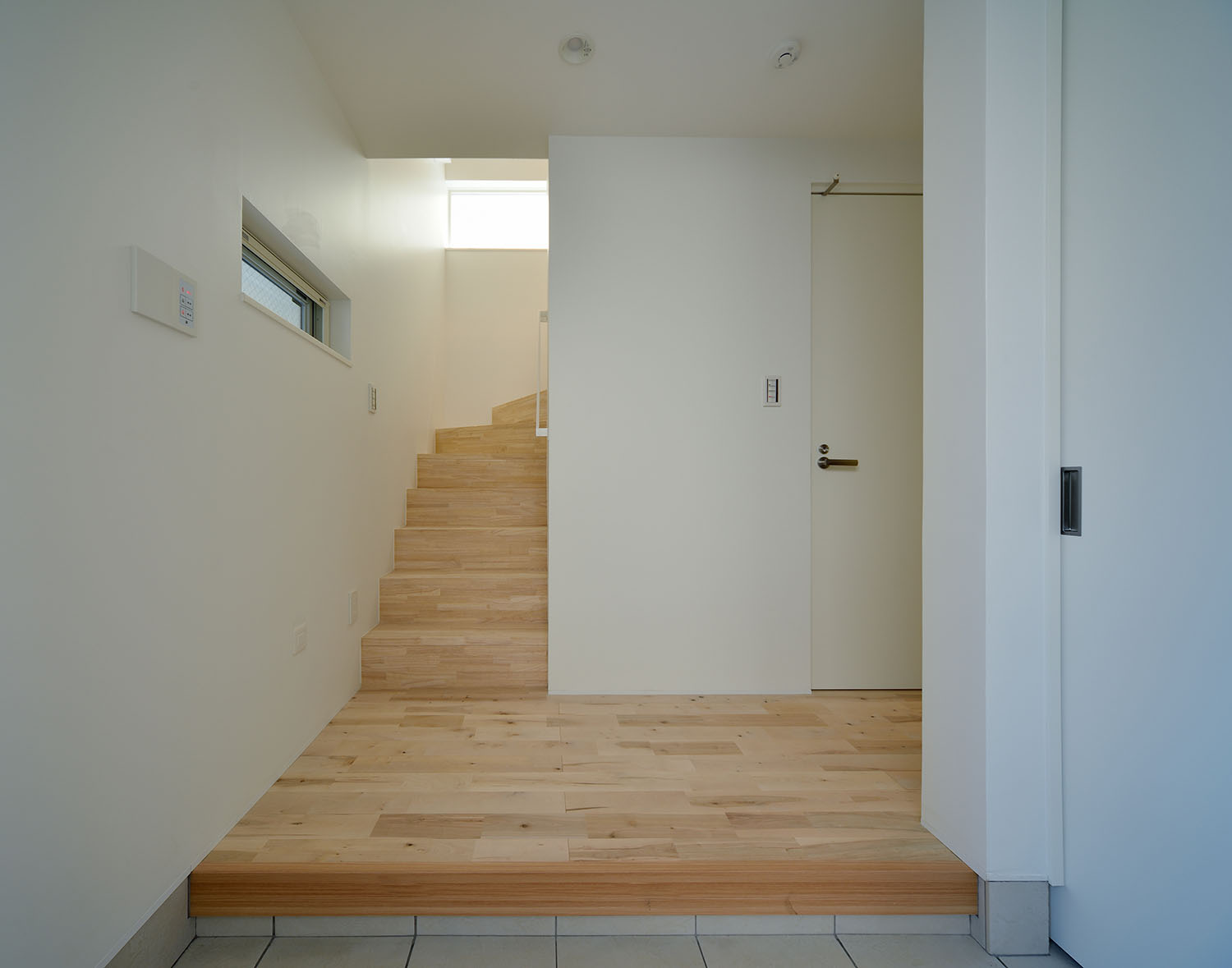 正面に木製の箱型階段があるシンプルな玄関・デザイン住宅