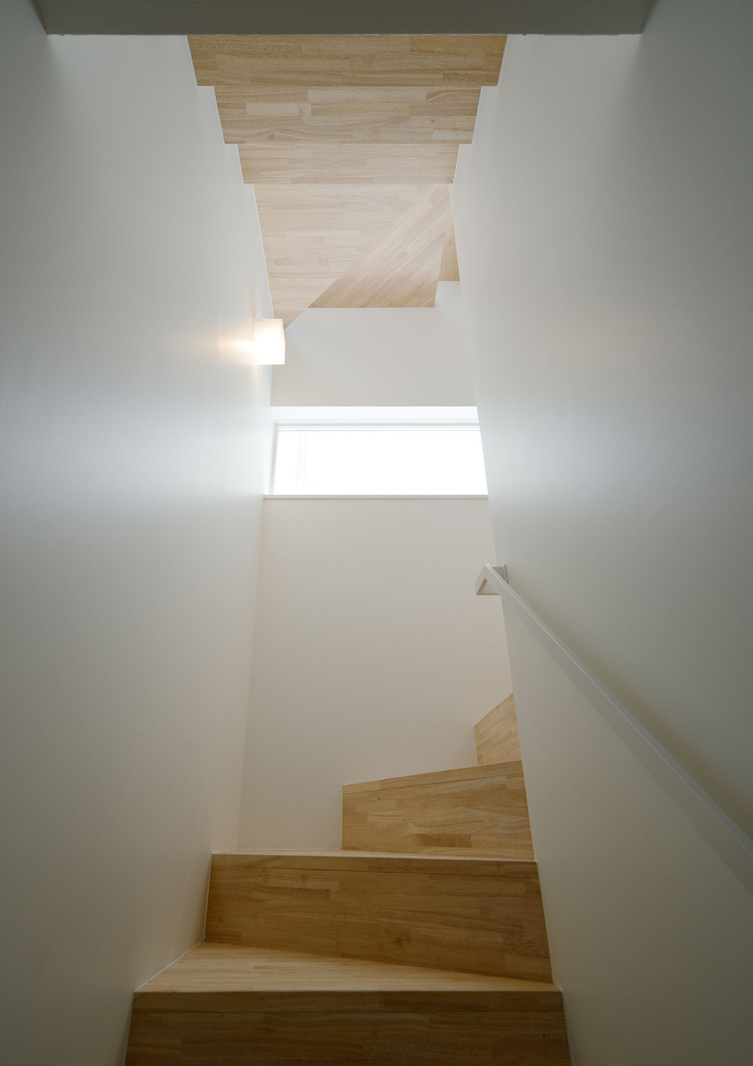 スリット窓が取り付けられた白い壁に囲まれた階段室・デザイン住宅