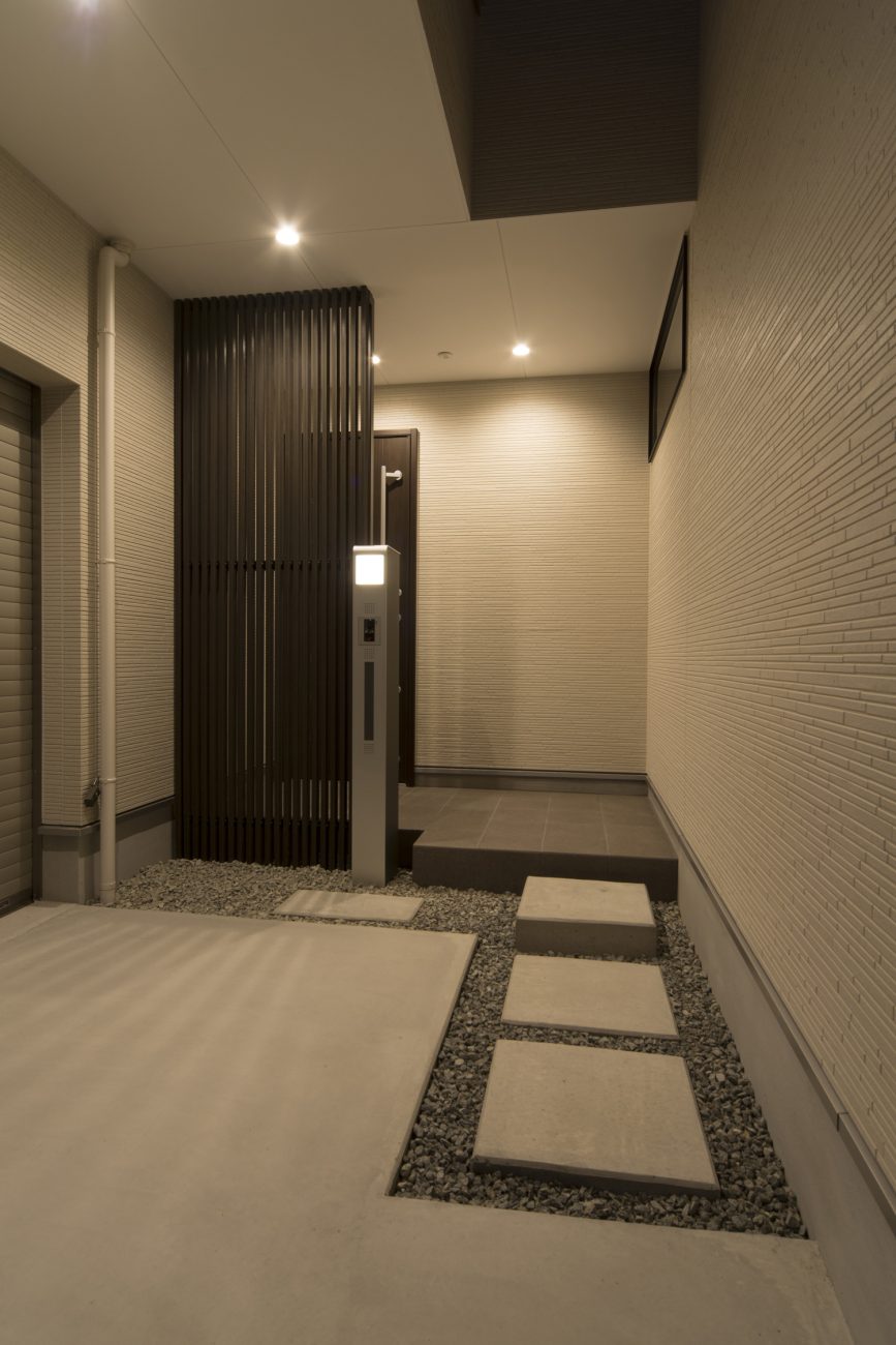 白い壁に黒いルーバーの目隠しを取り付けたモノトーンでプライベートな玄関・デザイン住宅