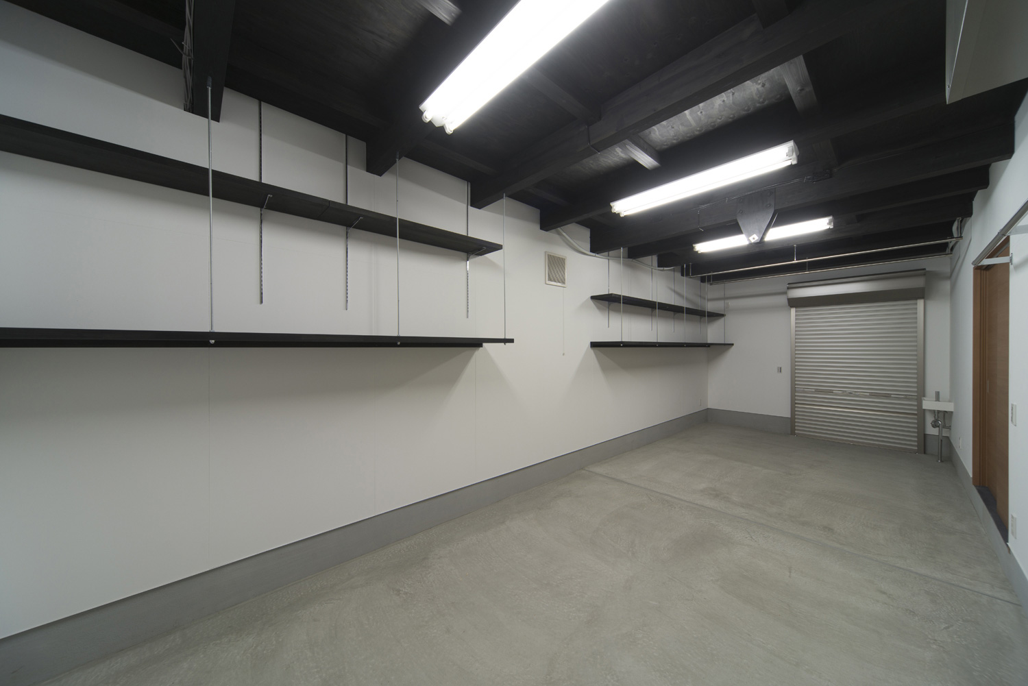 壁に可動棚を取り付けた広いガレージ・デザイン住宅