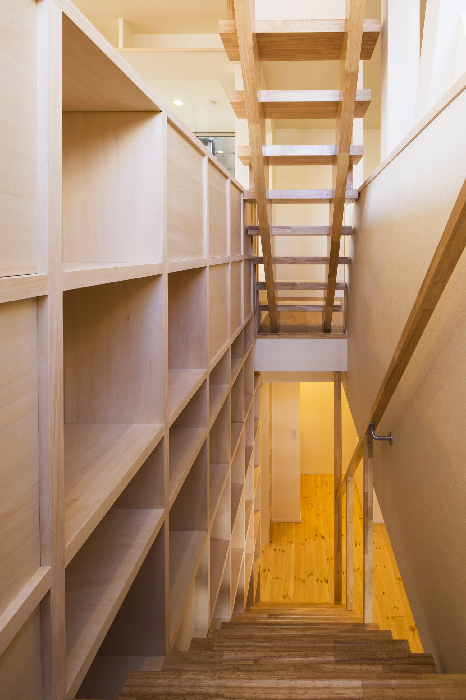 壁に木製の収納棚が取り付けられた吹き抜けの階段室・デザイン住宅