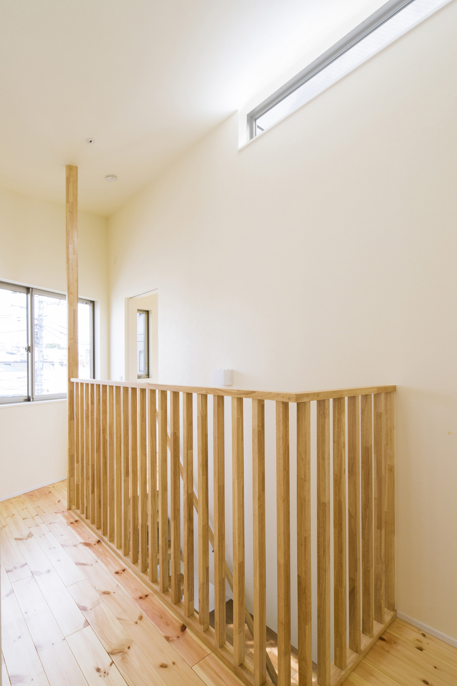 天井近くにスリット窓が取り付けられた木の柵付きの明るい廊下・デザイン住宅