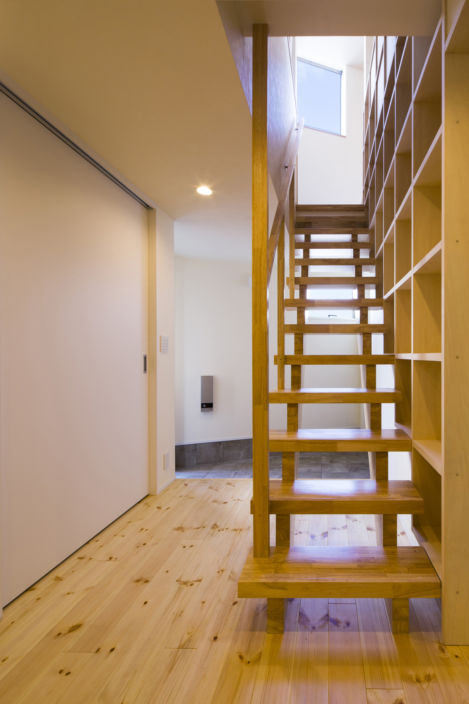 木製のスケルトン階段越しに見える玄関・デザイン住宅