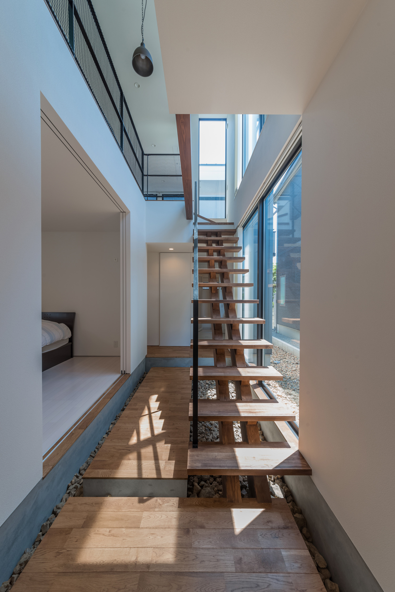 大きな窓に面した吹き抜け部分にある木製のスケルトン階段・デザイン住宅