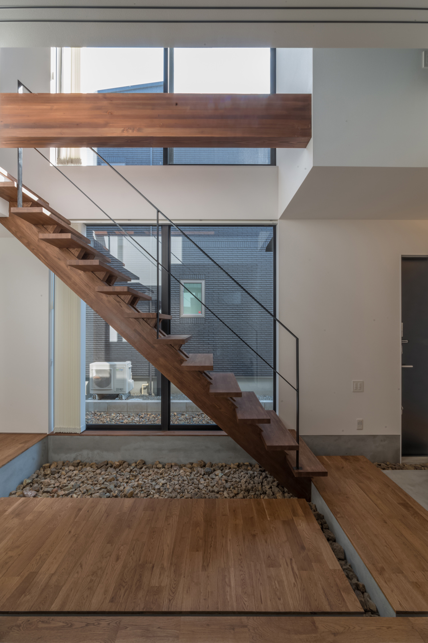 木製のスケルトン階段の下に石を敷き詰めた廊下・デザイン住宅