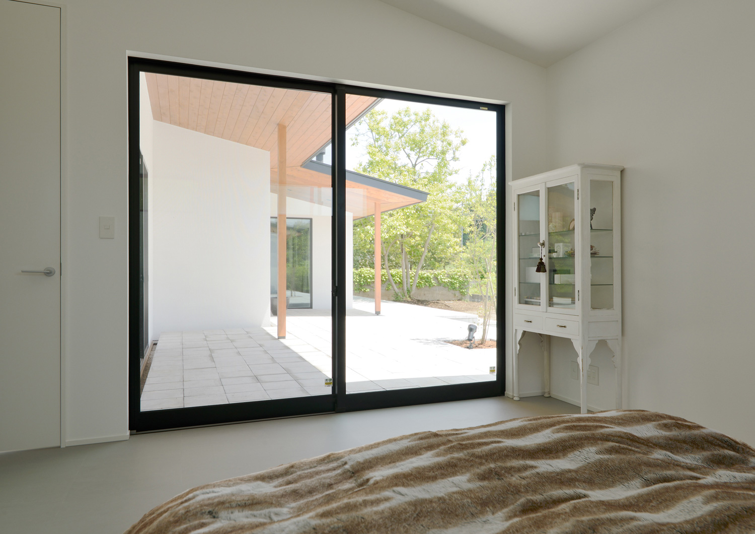 テラスとフラットに繋がる大きな窓がある開放的な寝室・デザイン住宅