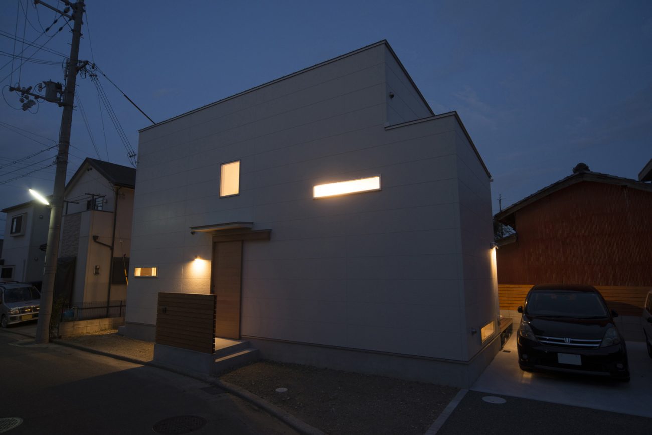 窓から光が漏れるシンプルな外観の家・デザイン住宅