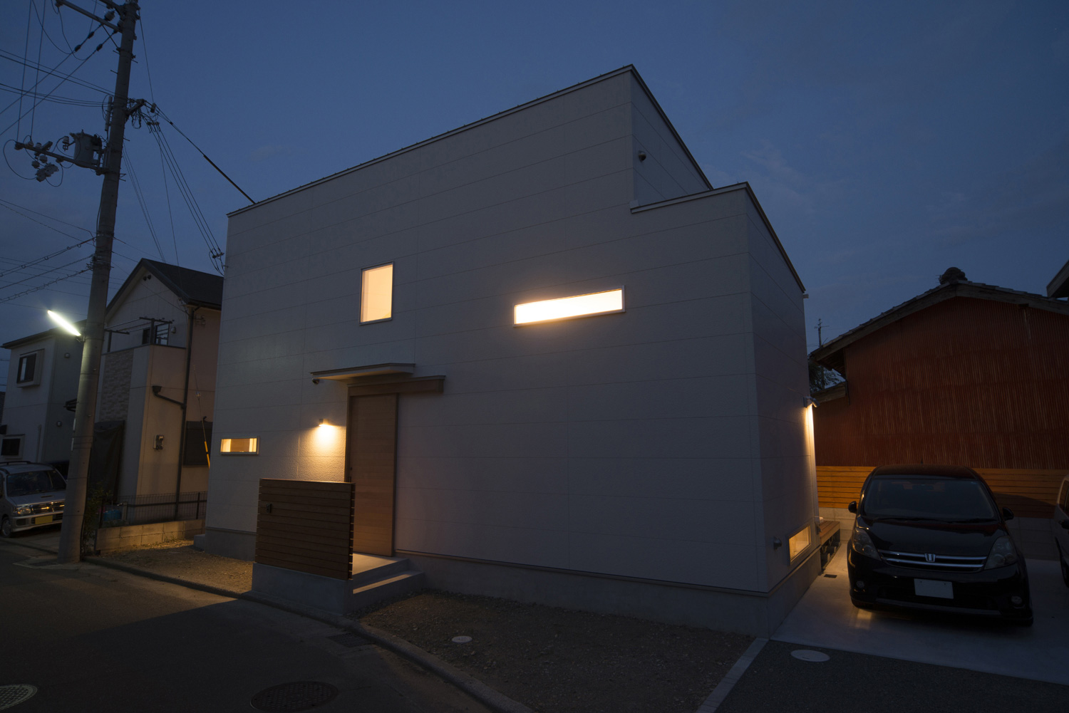 窓から光が漏れるシンプルな外観の家・デザイン住宅