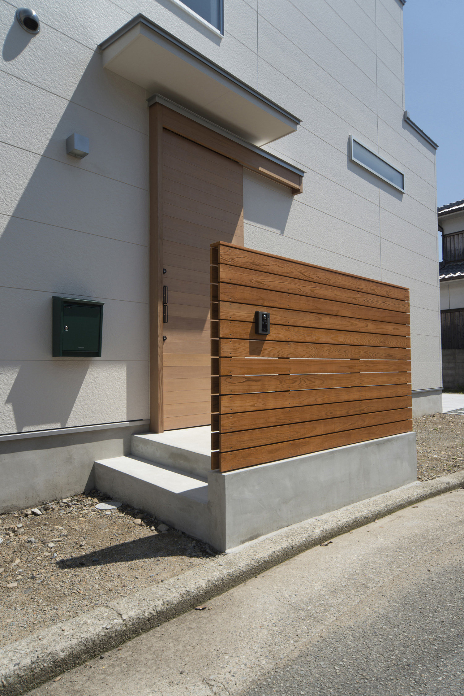 アプローチに木の目隠し壁が取り付けられている白い外壁の家・デザイン住宅