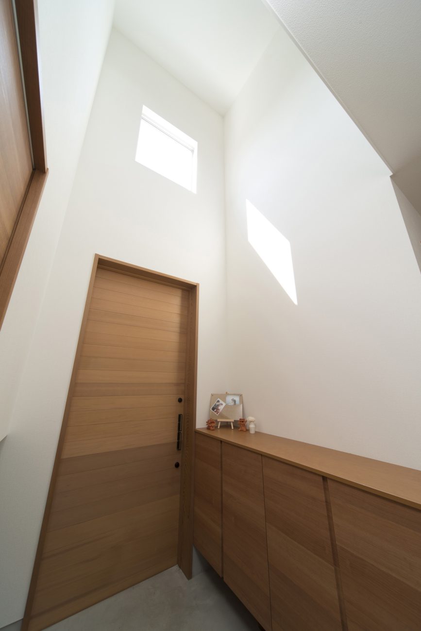 吹き抜けになった木のシューズボックスがある玄関・デザイン住宅