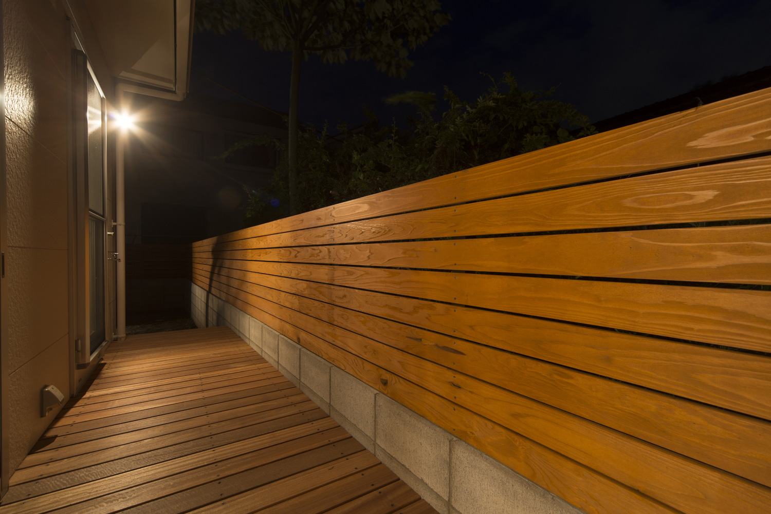 壁に照明が取り付けられた木の目隠し付きのテラス・デザイン住宅