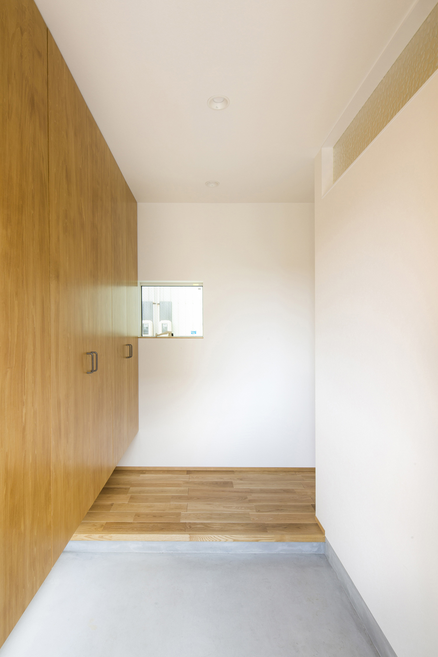 木の壁面収納があるモルタルのシンプルな玄関・デザイン住宅