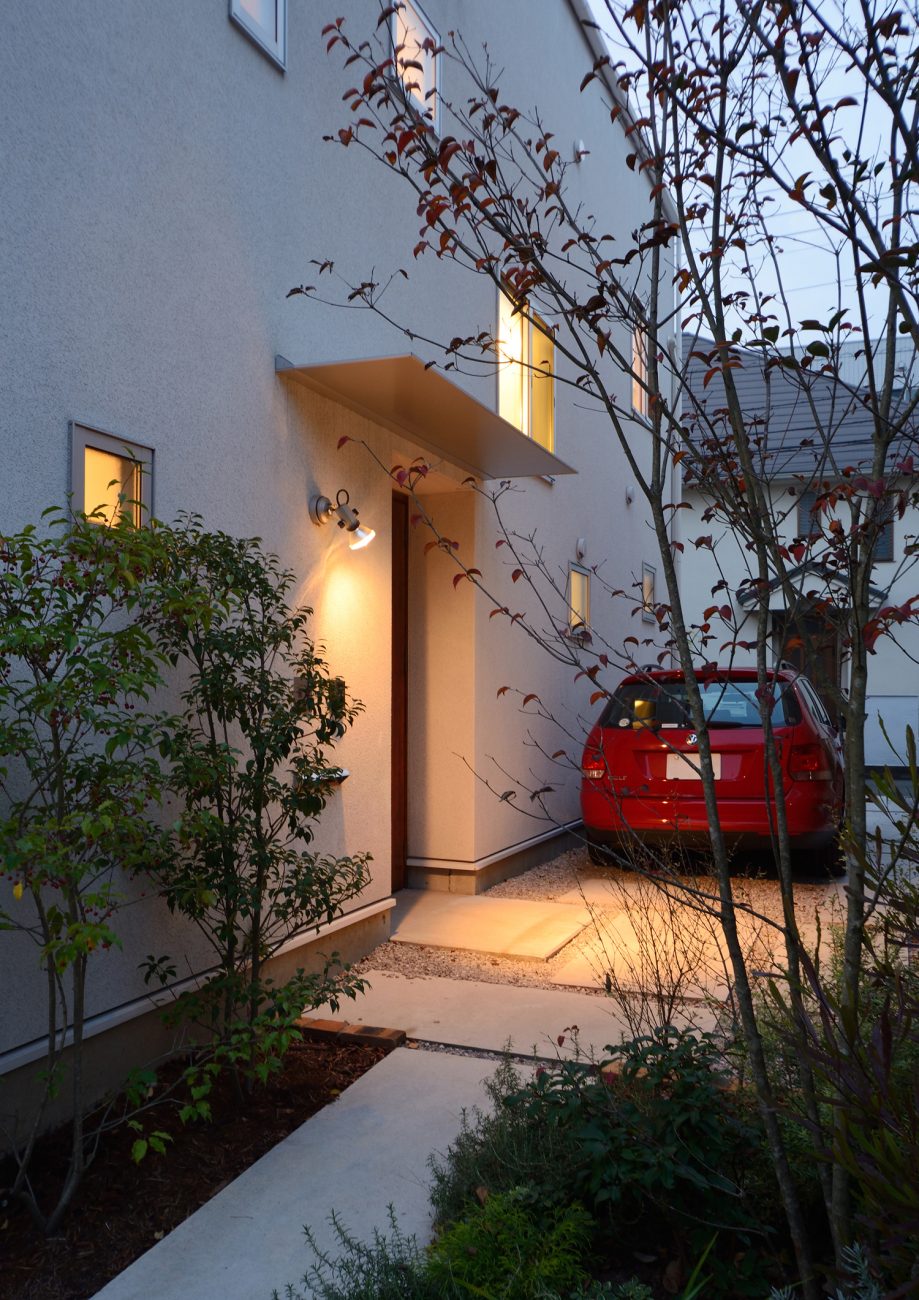 壁に照明を取り付けたシャープな庇がある玄関ポーチ・デザイン住宅